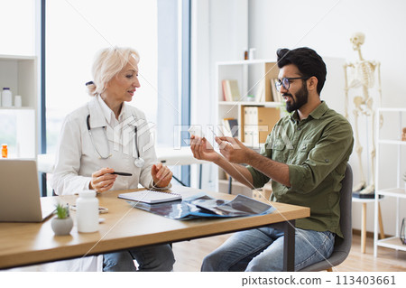 Senior female general practitioner communicating with young patient. 113403661