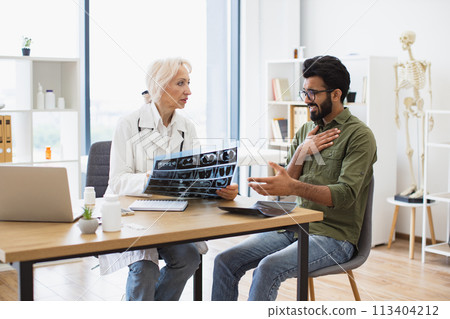 Mindful gray-haired female in lab coat holding MRI scan. 113404212