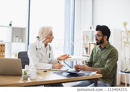 Gentleman describing symptoms of illness to senior female doctor. 113404253