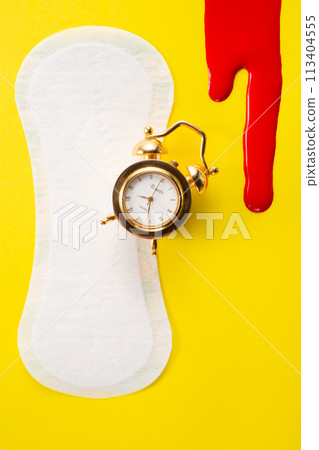 Blood, alarm clock and feminine hygiene pad with red glitter on yellow background. First menstrual period concept Blood, alarm clock and feminine hygiene pad with red glitter on yellow background. First menstrual period concept 113404555