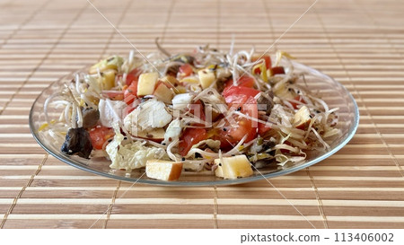 Salad of fresh vegetables and microgreens. Tomatoes, onions, apples, a mound of sprouted mung beans, sesame seeds, flax and cheese cubes on on a transparent plate on the table. Close-up Salad of fresh vegetables and microgreens. Tomatoes, onions, apples, a mound of sprouted mung beans, sesame seeds, flax and cheese cubes on on a transparent plate on the table. Close-up 113406002