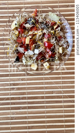 Salad of fresh vegetables and microgreens. Tomatoes, onions, apples, a mound of sprouted mung beans, sesame seeds, flax and cheese cubes on on a transparent plate on the table. Close-up Salad of fresh vegetables and microgreens. Tomatoes, onions, apples, a mound of sprouted mung beans, sesame seeds, flax and cheese cubes on on a transparent plate on the table. Close-up 113406005