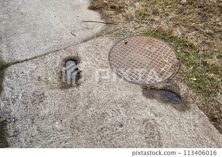 A rusty iron hatch with a pattern with a large gap at the top is mounted in the asphalt pavement of the pedestrian road. Close-up 113406016