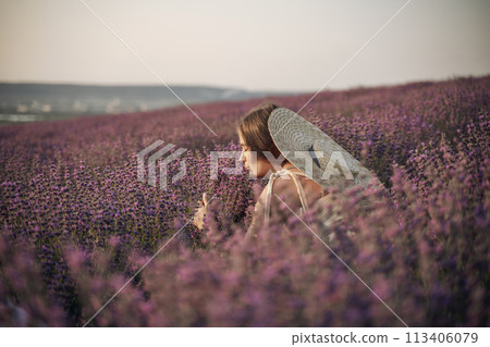 A woman is sitting in a field of lavender flowers. She is wearing a straw hat and holding a basket of flowers. The scene is peaceful and serene, with the woman enjoying the beauty of the flowers. A woman is sitting in a field of lavender flowers. She is wearing a straw hat and holding a basket of flowers. The scene is peaceful and serene, with the woman enjoying the beauty of the flowers. 113406079