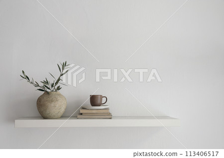 Elegant home still life. Floating shelf. Textured vase with green olive tree branches and old books. Cup of coffee, tea. Modern Mediterranean appartement. White wall background. Interior indoor mockup Elegant home still life. Floating shelf. Textured vase with green olive tree branches and old books. Cup of coffee, tea. Modern Mediterranean appartement. White wall background. Interior indoor mockup 113406517