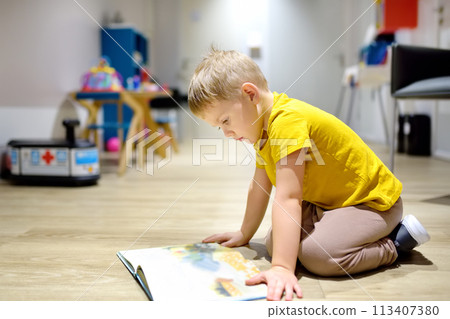 Cute little boy reading a book on the floor in a kindergarten. The child has time in the preschool 113407380