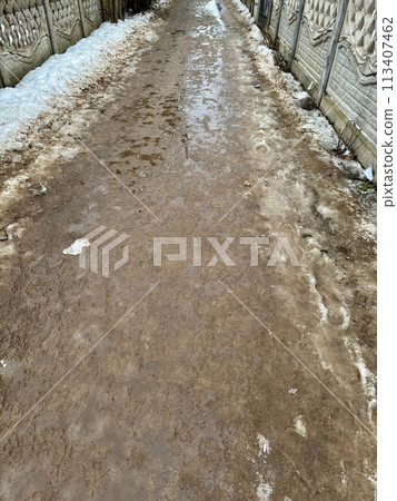 Melting dirty snow on the streets of the city during the daytime in winter. The pedestrian road is snow with sand and mud. Traces of people and pets. Melting dirty snow on the streets of the city during the daytime in winter. The pedestrian road is snow with sand and mud. Traces of people and pets. 113407462