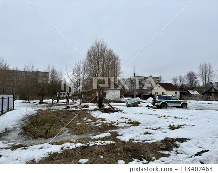 A white-blue SUV stuck in a picturesque snowy field with scattered trees and plants, creating a serene natural landscape under the overcast sky A white-blue SUV stuck in a picturesque snowy field with scattered trees and plants, creating a serene natural landscape under the overcast sky 113407463