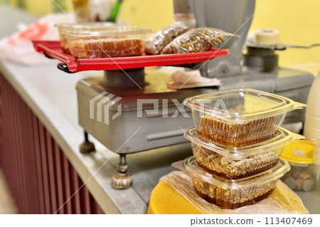Honeycombs with honey in transparent plastic containers on the counter for sale lie next to the scales. Wax structures made of honey in the food market 113407469