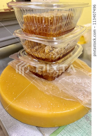 Honeycombs with honey in transparent plastic containers on the counter for sale lie next to the scales. Wax structures made of honey in the food market 113407496