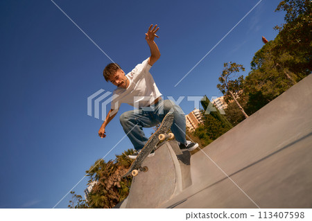 Full body of young male skater in casual outfit doing trick on skateboard riding in skate park Full body of young male skater in casual outfit doing trick on skateboard riding in skate park 113407598