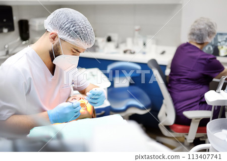 Dentist and patient at modern medical center. Doctor treats a young woman teeth in hospital. Practitioner examines the patient before orthodontists or prosthetics treatment. 113407741