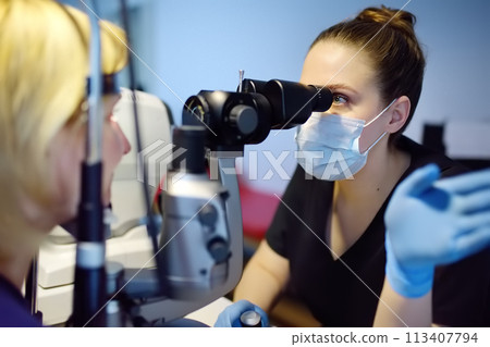 Slit Lamp eye examination with ophthalmologist. Patient during visit by oculist for exam of biomicroscopic analysis of eyelids, sclera, conjunctiva, iris, lens, cornea. Checkup of retina and fundus 113407794