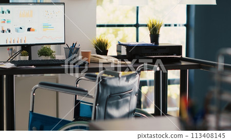 Wheelchair in inclusive office for employees and computer screen showing statistics graphs. Medical chair in financial department workspace offering accessibility to workers with disability Wheelchair in inclusive office for employees and computer screen showing statistics graphs. Medical chair in financial department workspace offering accessibility to workers with disability 113408145
