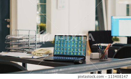 Company documents and laptop in financial department office showing stock exchange values. Business files on desk next to notebook showing forex trading indexes prices, panning shot 113408147