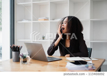 Overwhelmed businesswoman holds her head in distress while working on a laptop at her desk in a contemporary office. 113408892