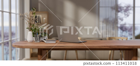 A laptop computer and decor on a wooden table by the window in a cozy contemporary room. 113411018