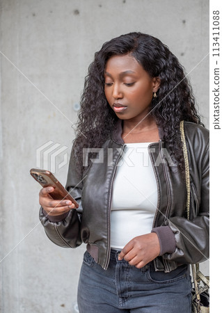 Young African Woman in Leather Jacket Engrossed in Smartphone Young African Woman in Leather Jacket Engrossed in Smartphone 113411088