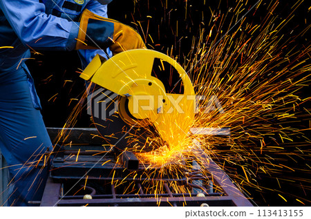 Worker man in blue uniform with yellow leather gloves cutting metal pipe by electric circular abrasive saw with sparks. Metal working with personnel protective equipment. . 113413155
