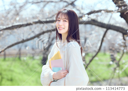 A woman walking along a riverbed of cherry blossom trees 113414773