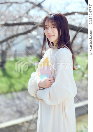 A woman walking along a riverbed of cherry blossom trees 113414777