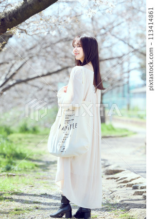A woman walking along a riverbed of cherry blossom trees 113414861