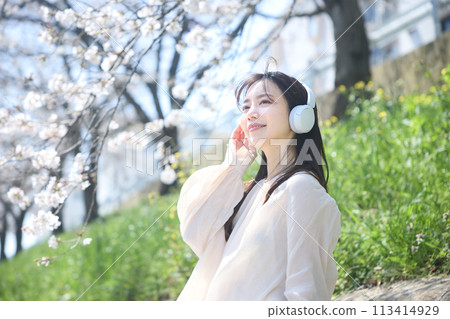 A woman listening to music under the cherry blossoms 113414929