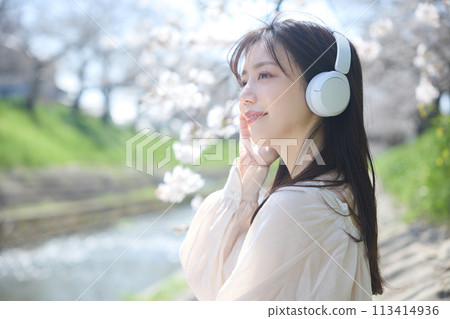 A woman listening to music under the cherry blossoms 113414936