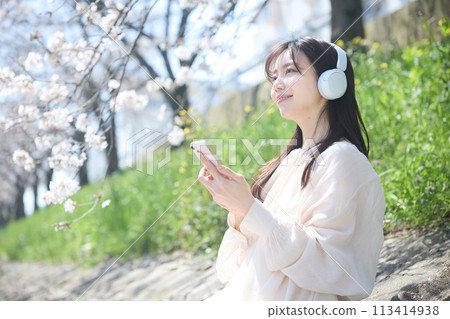 A woman listening to music under the cherry blossoms 113414938