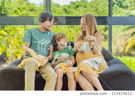 Heartwarming family moment as expectant mom, dad, and son joyfully browse through newborn baby's clothes, eagerly anticipating the arrival of a new family member 113415613