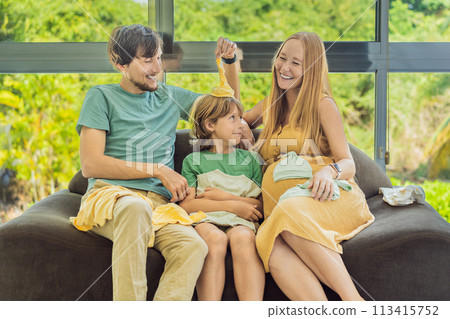 Heartwarming family moment as expectant mom, dad, and son joyfully browse through newborn baby's clothes, eagerly anticipating the arrival of a new family member 113415752