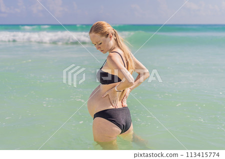 In the sea, a pregnant woman experiences a moment of discomfort as she stands, gently tending to her back, highlighting the challenges of back pain during pregnancy In the sea, a pregnant woman experiences a moment of discomfort as she stands, gently tending to her back, highlighting the challenges of back pain during pregnancy 113415774