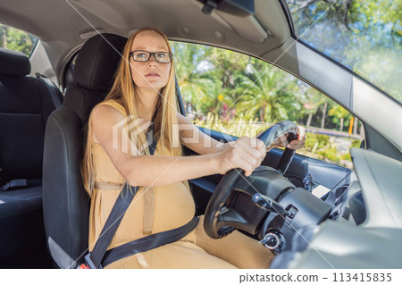 Pregnant woman driving with safety belt on in the car. Confident and capable, a pregnant woman takes the wheel, driving with care and determination as she navigates the journey of motherhood Pregnant woman driving with safety belt on in the car. Confident and capable, a pregnant woman takes the wheel, driving with care and determination as she navigates the journey of motherhood 113415835