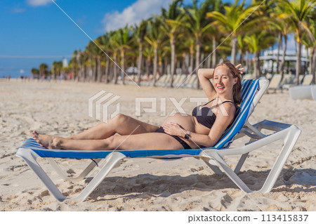 Basking in seaside tranquility, a pregnant woman lounges on a sun lounger, embracing the soothing ambiance of the beach for a moment of serene relaxation 113415837