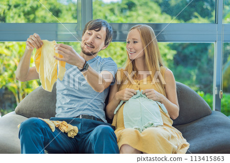 In a heartwarming scene, the future mom and dad hold their unborn baby's clothes in their hands, savoring the joy of anticipation and shared excitement for their little one's arrival In a heartwarming scene, the future mom and dad hold their unborn baby's clothes in their hands, savoring the joy of anticipation and shared excitement for their little one's arrival 113415863