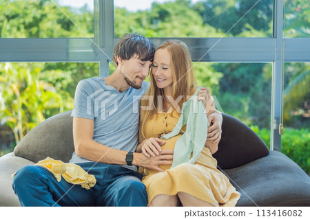 In a heartwarming scene, the future mom and dad hold their unborn baby's clothes in their hands, savoring the joy of anticipation and shared excitement for their little one's arrival In a heartwarming scene, the future mom and dad hold their unborn baby's clothes in their hands, savoring the joy of anticipation and shared excitement for their little one's arrival 113416082