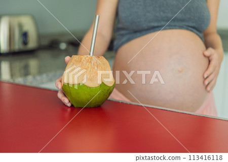 Quenching her pregnancy thirst with a refreshing choice, a pregnant woman joyfully drinks coconut water from a coconut in the kitchen, embracing natural hydration during this special journey Quenching her pregnancy thirst with a refreshing choice, a pregnant woman joyfully drinks coconut water from a coconut in the kitchen, embracing natural hydration during this special journey 113416118