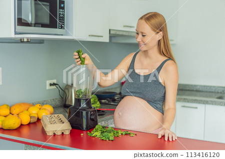 Embracing a nutritious choice, a pregnant woman joyfully prepares a vibrant vegetable smoothie, prioritizing wholesome ingredients for optimal well-being during her maternity journey 113416120