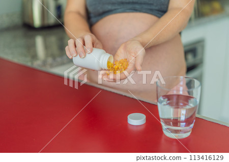 pregnant woman conscientiously takes fish oil capsules, rich in omega-3, prioritizing essential nutrients for a healthy pregnancy journey 113416129