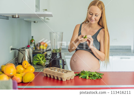 Embracing a nutritious choice, a pregnant woman joyfully prepares a vibrant vegetable smoothie, prioritizing wholesome ingredients for optimal well-being during her maternity journey 113416211