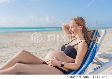 Basking in seaside tranquility, a pregnant woman lounges on a sun lounger, embracing the soothing ambiance of the beach for a moment of serene relaxation 113416339
