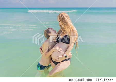 A picturesque moment: a pregnant woman and her son enjoying the turquoise sea, a heartwarming family bond by the tranquil shore 113416357