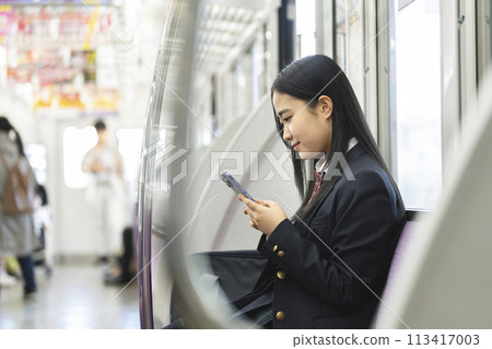 High school girl looking at smartphone screen on train - Image of commuting to school by train 113417003