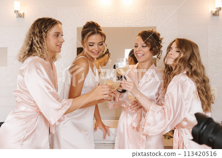 Three bridesmaids with bride are opening champagne and drinking in bathroom. Wedding morning mood of bride Three bridesmaids with bride are opening champagne and drinking in bathroom. Wedding morning mood of bride 113420516