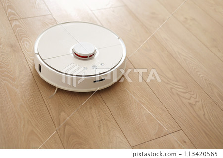 Top view of white wireless autonomous robotic vacuum cleaner on wooden floor. Smart cleaning technology. Self-propelled cleaning robot. Floor cleaning system. Household remote control appliances. 113420565