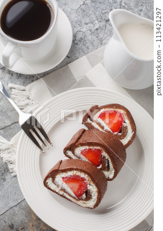 Sweet chocolate cake roll filled with strawberries and cream cheese served with coffee close-up. Vertical top view 113421297