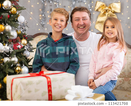 Happy father with son and daughter near the Christmas tree in living room. Merry Christmas Happy father with son and daughter near the Christmas tree in living room. Merry Christmas 113421708