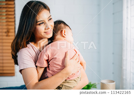In the comfort of their home an Asian mom leans in to cuddle her tiny peacefully sleeping infant celebrating a heartwarming family moment filled with awe of childbirth and the innocence of childhood. 113422165