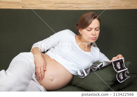Expectant mother looking at sonograms on couch 113422566