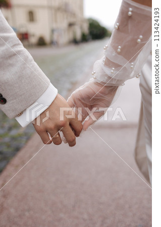 Close-up of groom holds bride's hand. Wedding couple walking in the centre of the city  113424193